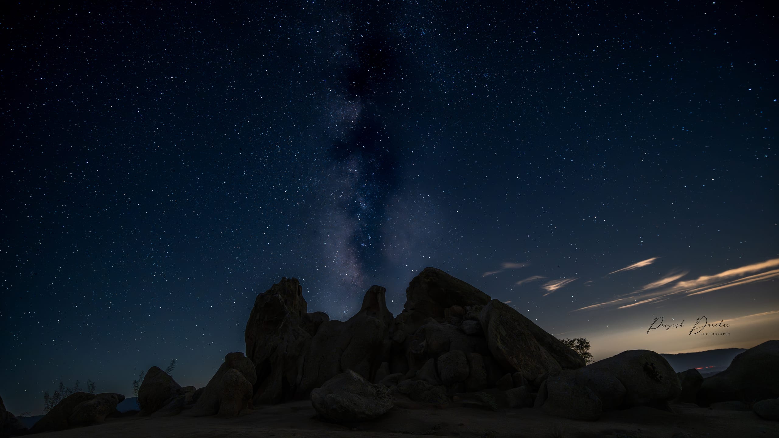 The Milky Way arcing above a dark granite rock formation under a sky thick with stars.