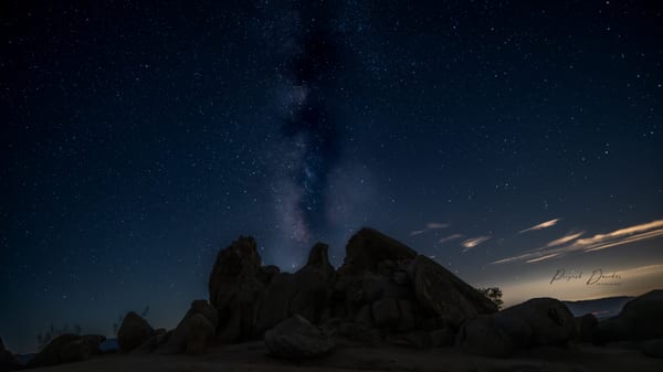 The Milky Way arcing above a dark granite rock formation under a sky thick with stars.