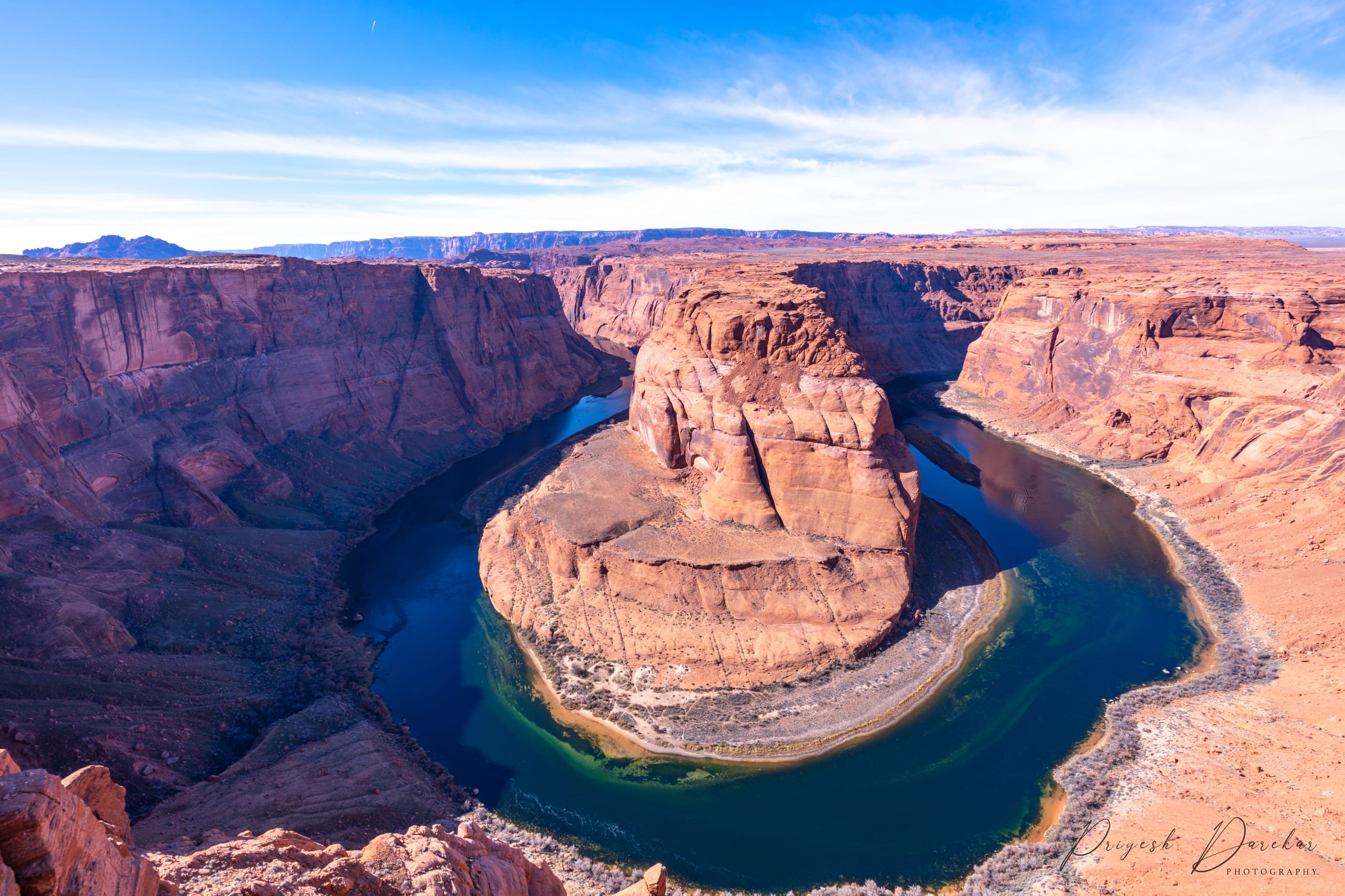 The Colorado River wrapped in a full horseshoe around a red sandstone butte, seen from the canyon rim.