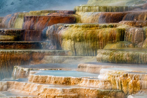 Stepped travertine terraces in white and ochre, thin water spilling over each lip into the pool below.